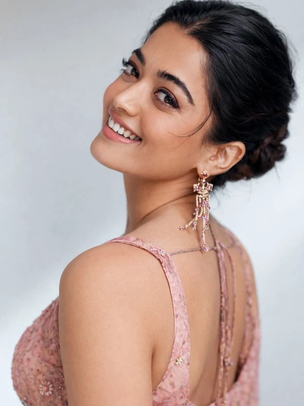 Smiling woman in a pale pink embroidered dress looking over her shoulder